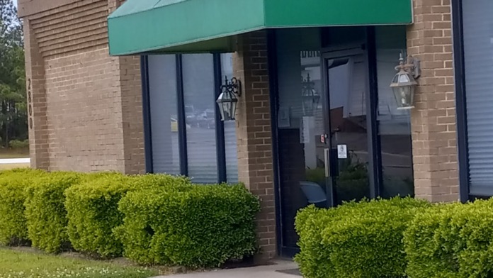 Exterior entrance featuring brick facade, green canvas awning, glass entry doors, and manicured landscape
