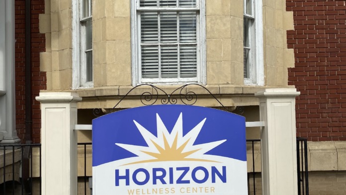 Exterior front entrance of Horizon Wellness Center showing cream and brick facade with blue logo sign and landscaped grounds