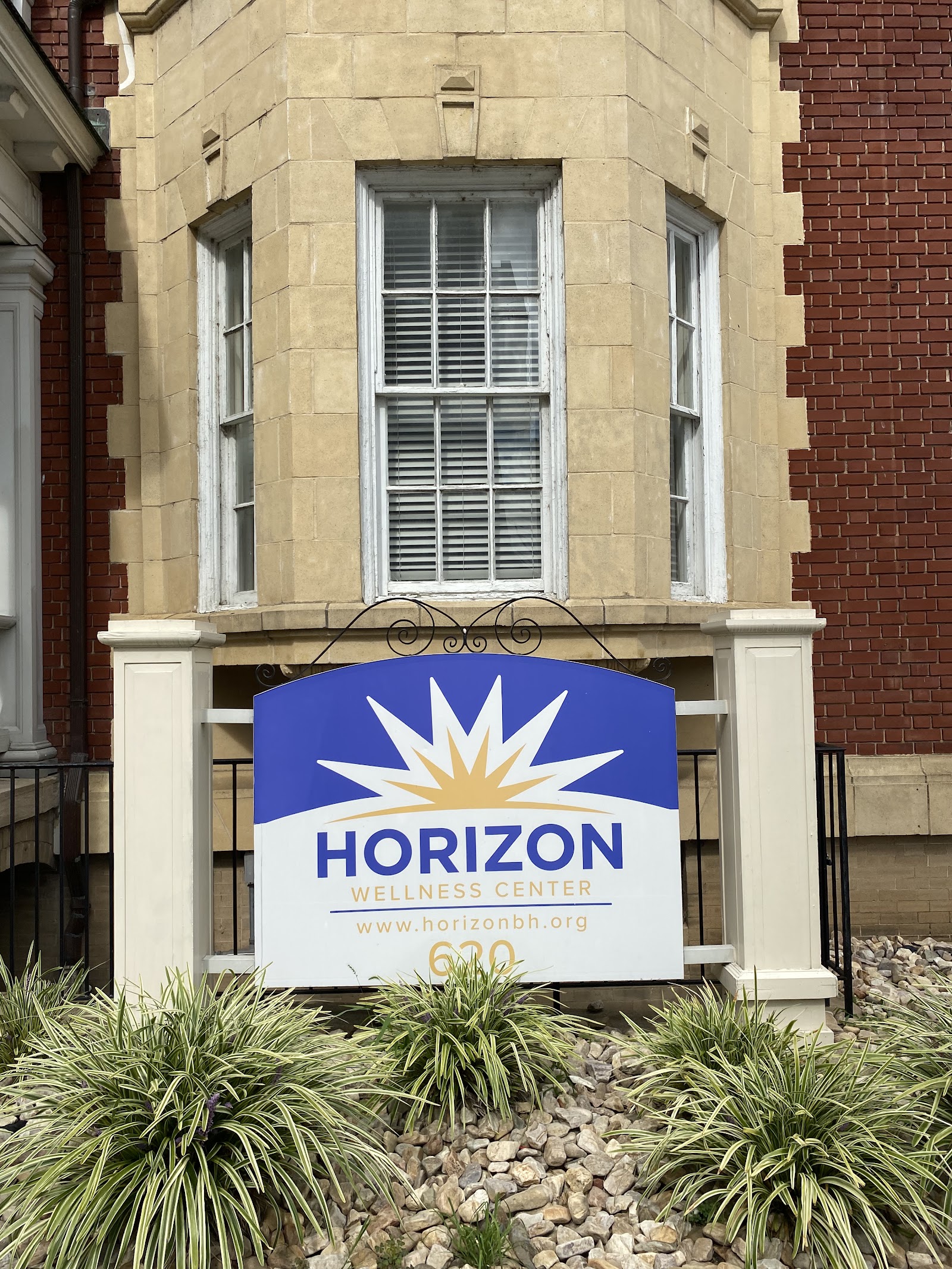 Exterior front entrance of Horizon Wellness Center showing cream and brick facade with blue logo sign and landscaped grounds