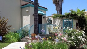 Exterior view of treatment center entrance featuring turquoise accents, flowering gardens, palm trees, and welcoming courtyard with accessible ramp