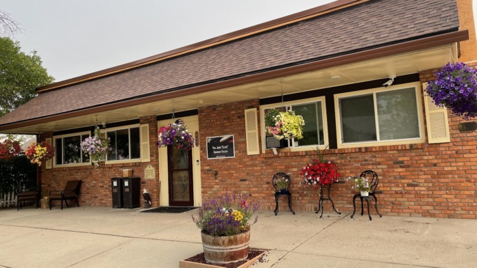 Exterior front entrance of brick treatment facility with colorful hanging flower baskets, covered patio area, and welcoming entrance door