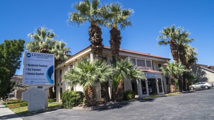 Exterior front of treatment facility showing entrance, red tile roof, palm trees, landscaping, and parking area