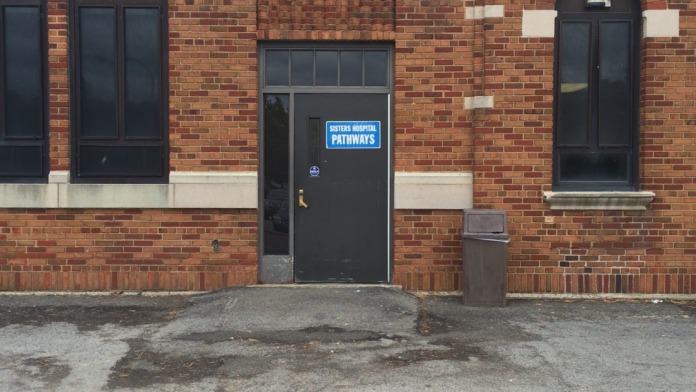 Exterior front entrance of brick building showing black door with blue Pathways signage and parking area markings