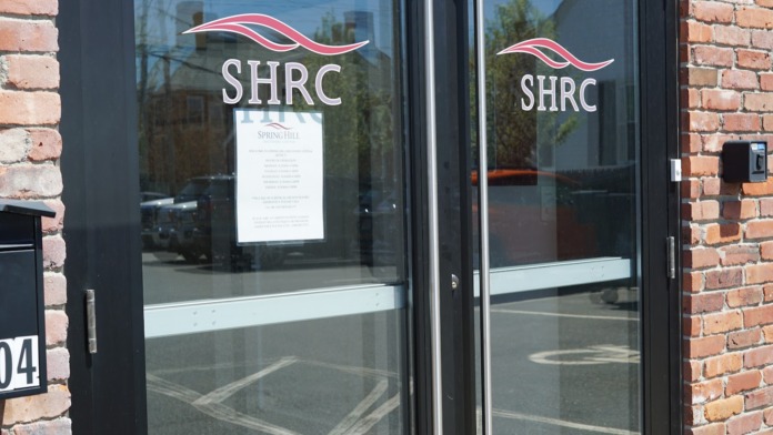 Exterior view of facility entrance showing SHRC logo on glass doors with brick facade and address marker