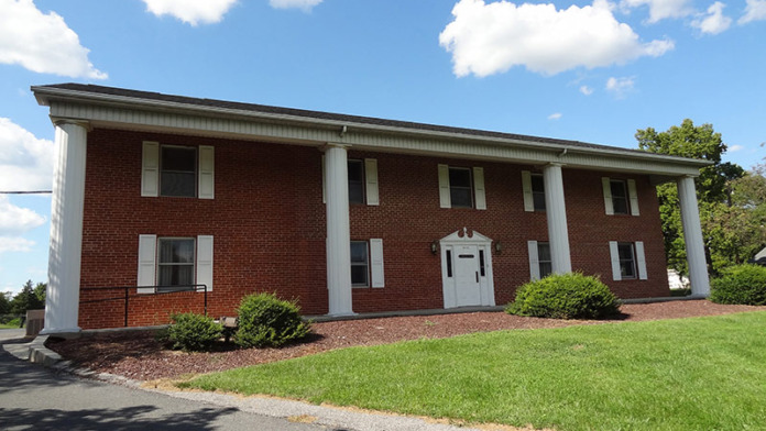 Exterior view of brick treatment center building with white columns, multiple windows, landscaped grounds, and clear sky