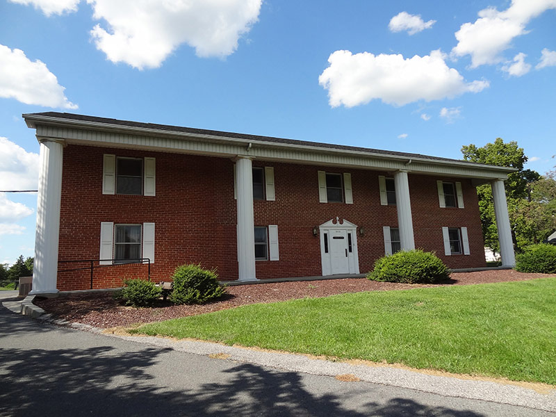 Exterior view of brick treatment center building with white columns, multiple windows, landscaped grounds, and clear sky