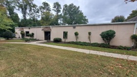 Exterior view of single-story treatment facility with cream-colored brick facade, landscaped grounds, and manicured lawn area
