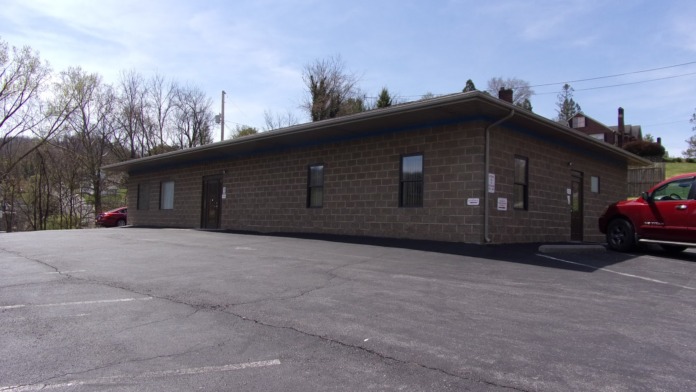 Exterior view of single-story brick medical facility with parking area, entrance, and surrounding landscape on hillside