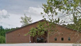 Exterior view of brick treatment center building with parking area, landscaping, and natural surroundings