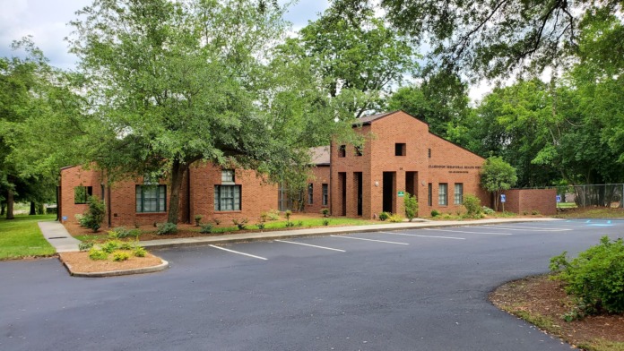 Exterior of brick behavioral health facility surrounded by mature trees, landscaping, and paved driveway