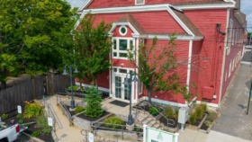 Exterior view of red historic building with white trim, entrance with railings, landscaping, and Pine Tree signage
