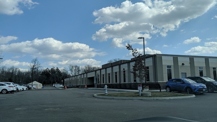 Exterior view of mental health facility main building with gray metal construction, parking lot, landscaping, and facility signage