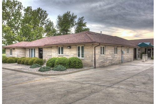 Exterior view of one-story brick health center with pitched roof, landscaped grounds, and wide paved driveway