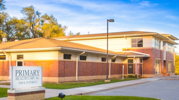 Exterior view of Primary Health Care facility showing brick facade, entrance with accessibility markings, and landscaped grounds