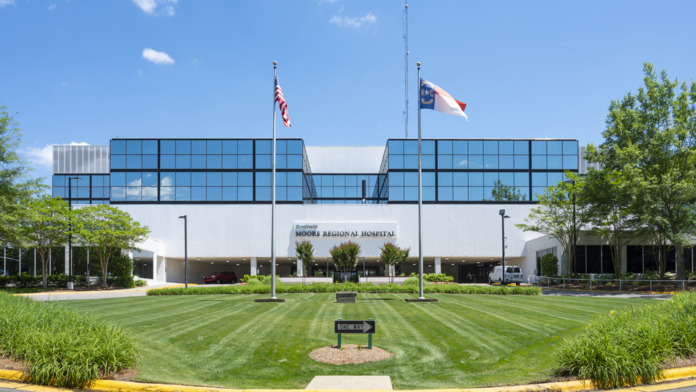 Exterior front view of hospital showing modern facade with blue glass upper floor, manicured lawn, flagpoles, and curved driveway approach
