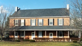 Exterior two-story brick farmhouse with white trim, shutters, front porch, and surrounding grounds