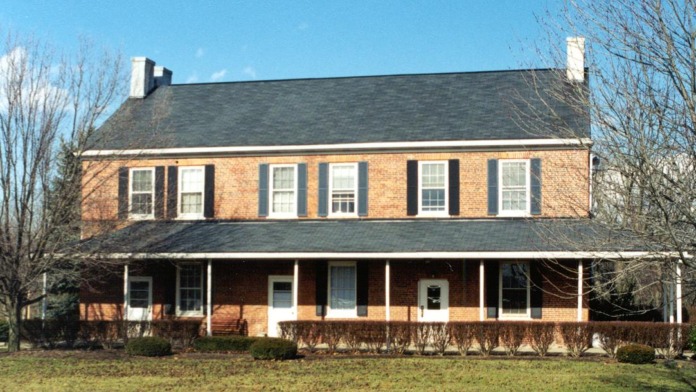 Exterior two-story brick farmhouse with white trim, shutters, front porch, and surrounding grounds