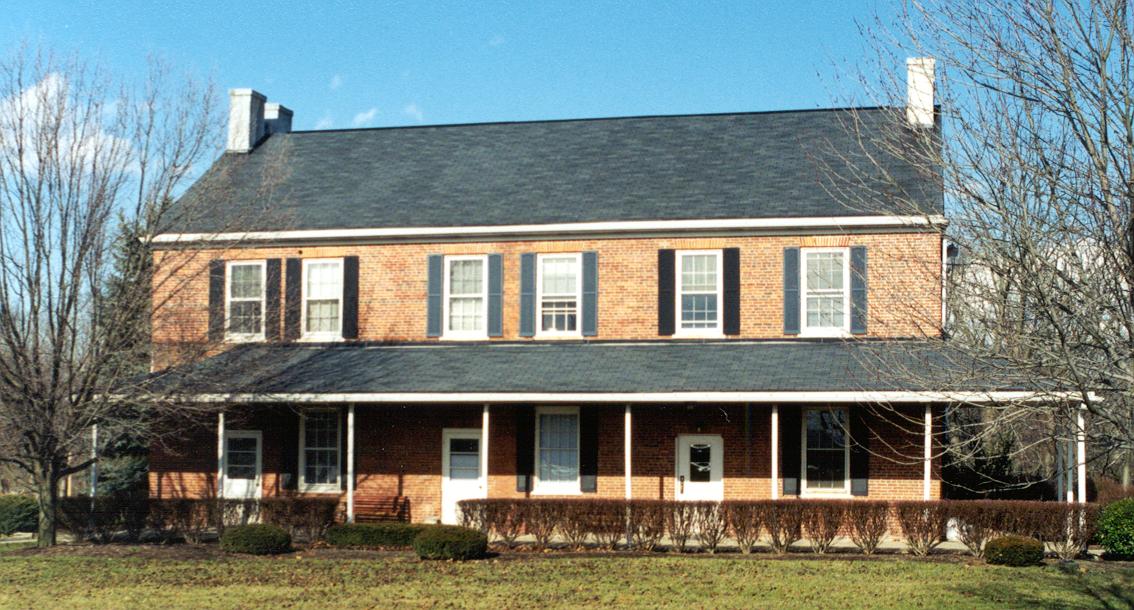 Exterior two-story brick farmhouse with white trim, shutters, front porch, and surrounding grounds