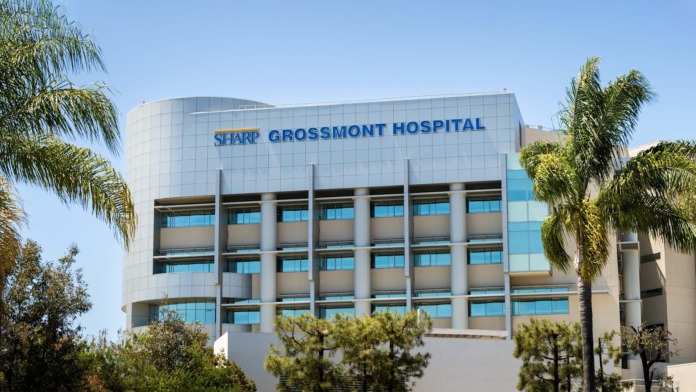 Exterior front view of modern hospital building with blue SHARP GROSSMONT HOSPITAL signage, curved white facade, and landscape plantings