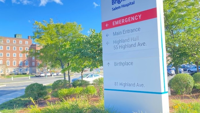 Exterior wayfinding sign directing to emergency, main entrance, and departments with landscaped grounds