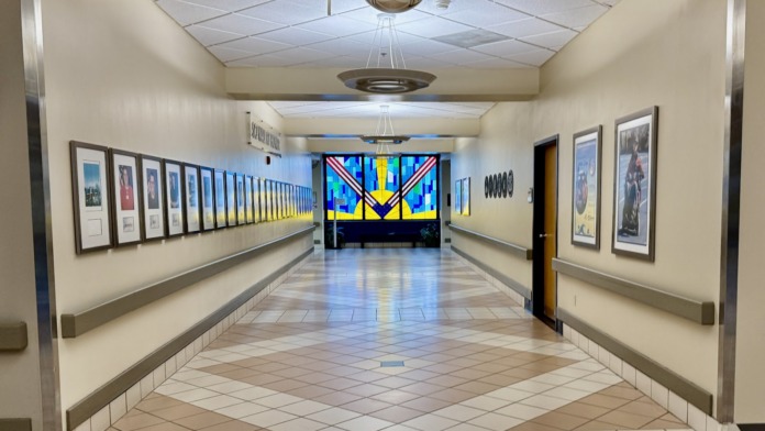 Interior hallway with framed artwork on walls, ceiling lights, and colorful display at end