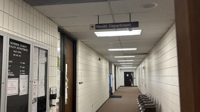 Interior hallway with white tile walls, directional signage, ceiling lights, and burgundy floor runner
