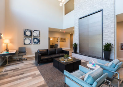 Interior lobby with contemporary furnishings, dark sofas, blue accent chairs, coffee table, and large windows with natural light