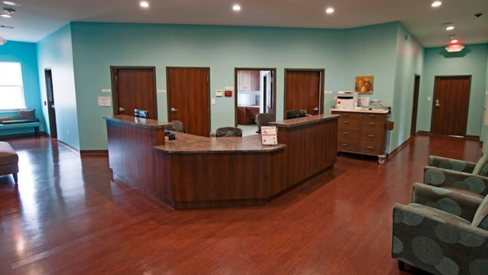 Interior spacious lobby with curved wooden reception desk, turquoise walls, multiple doorways, sitting area, and hardwood flooring
