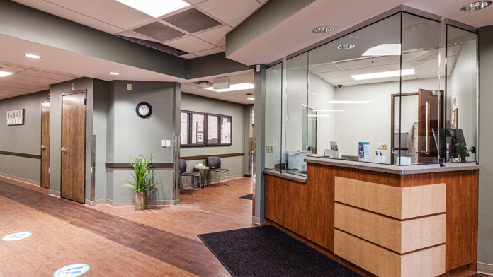 Interior main lobby with wooden reception desk, glass partitions, potted plant, and professional flooring