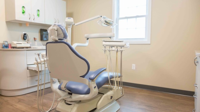 Interior medical treatment room with blue walls, examination chair, and clinical equipment including blood pressure monitors