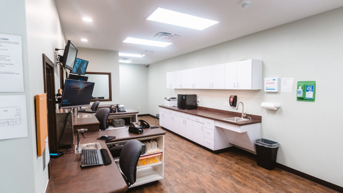 Interior clinical office with desk, computer monitors, white cabinets, and medical equipment