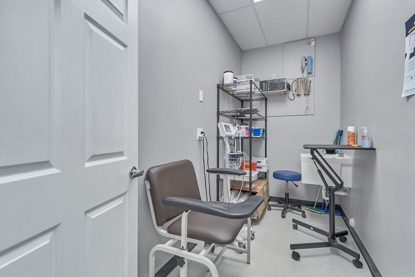 Interior clinical treatment room with examination chair, work surface, shelving with supplies, and medical equipment