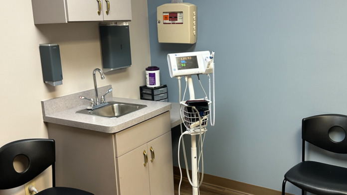 Interior treatment room with sink, medical equipment, cabinet, examination chair, and blood pressure monitor station.