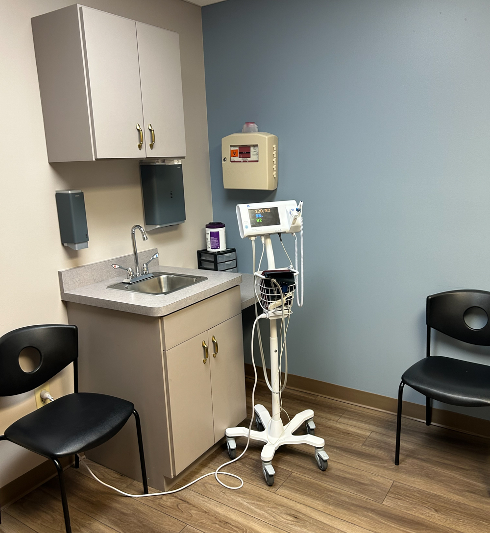 Interior treatment room with sink, medical equipment, cabinet, examination chair, and blood pressure monitor station.