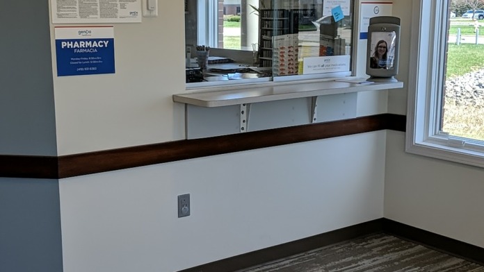 Interior pharmacy service window with Genoa Healthcare branding, medication display, and patient information materials