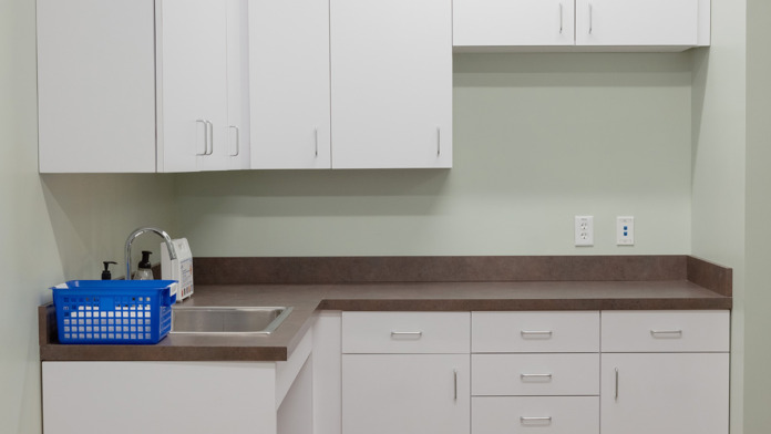 Interior clinical preparation area with white cabinets, sink, dark countertop, and storage supplies