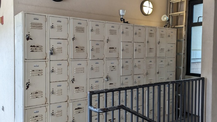 Interior hallway with rows of metal storage lockers, railings, and doors leading to facility areas