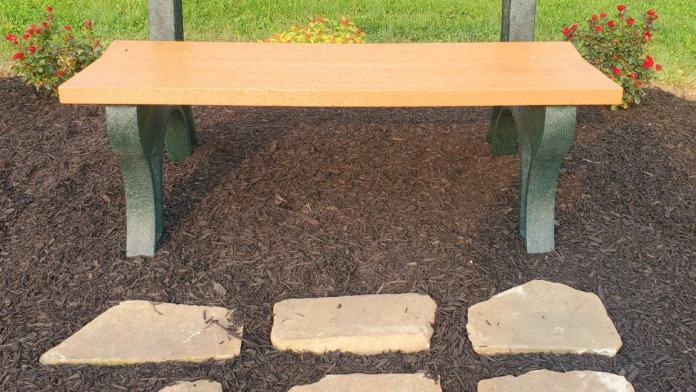 Outdoor memorial bench with plaque in landscaped garden setting with flowering plants and mulch bedding
