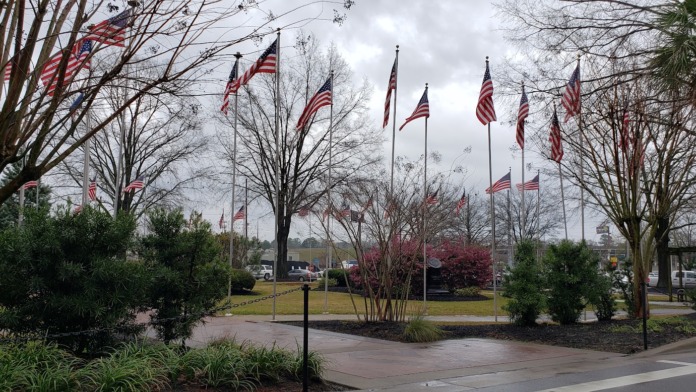 Outdoor grounds with multiple flagpoles displaying American flags, trees, and landscaping