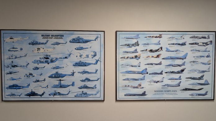 Interior wall display with framed educational charts showing military helicopters and warplanes with identification labels and specifications
