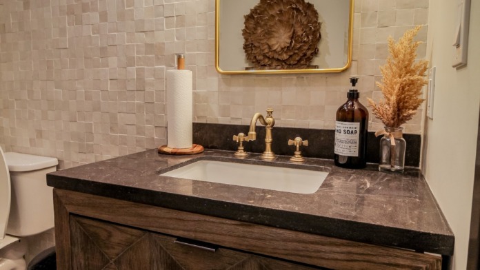 Interior bathroom with marble vanity, brass fixtures, mirror with lighting, and decorative accessories.