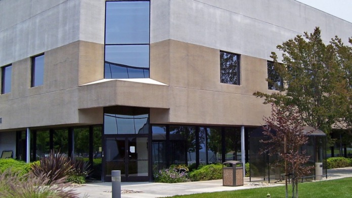 Exterior view of contemporary treatment facility building with concrete and stone facade, large windows, manicured landscaping, and paved walkway entrance
