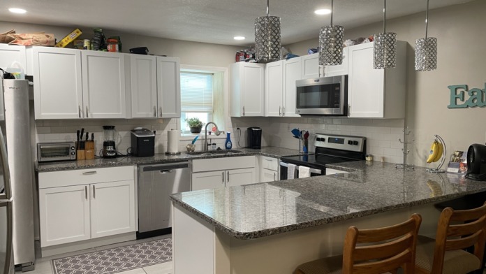 Interior kitchen with white cabinets, stainless steel appliances, granite countertop, pendant lighting, and dining area