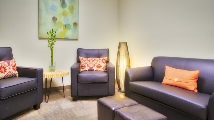 Interior lounge with purple upholstered chairs, decorative pillows, floor lamp, glass vase, abstract wall art, and neutral color palette