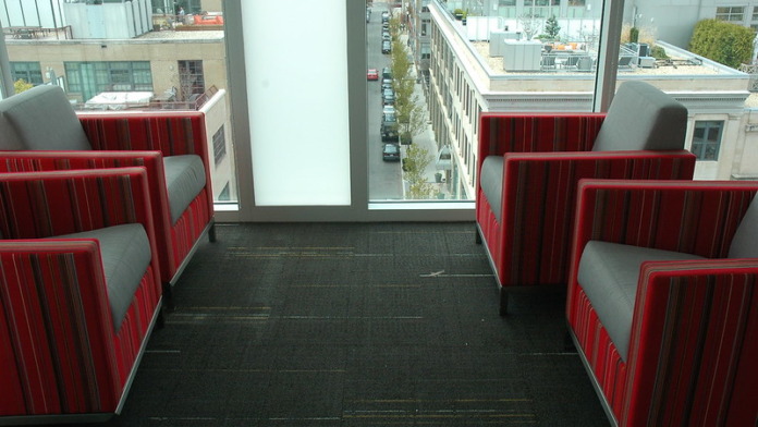 Interior lounge space with red and gray upholstered booth seating and large windows overlooking city streets