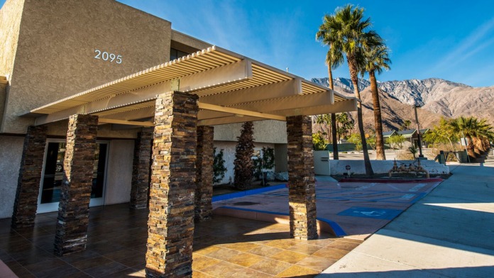 Exterior patio area with modern pergola design, stone support columns, address number 2095, metal railing, and palm trees visible
