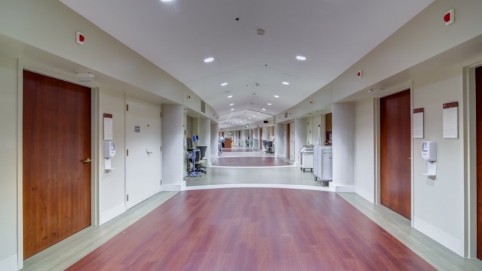 Interior hallway with white walls, red doors, recessed lighting, polished flooring and institutional clinical design