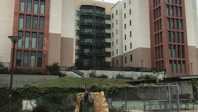 Exterior view of contemporary multi-story residential buildings with red brick and cream colored facade, featuring regular window patterns and residential design