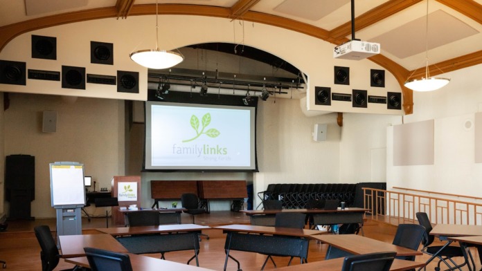 Interior large room with curved wooden ceiling beams, projection screen displaying FamilyLinks logo, tables, chairs, and audio equipment