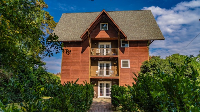 Exterior view of rustic multi-story building with distinctive A-frame design, balconies, brick construction, and surrounding landscaping